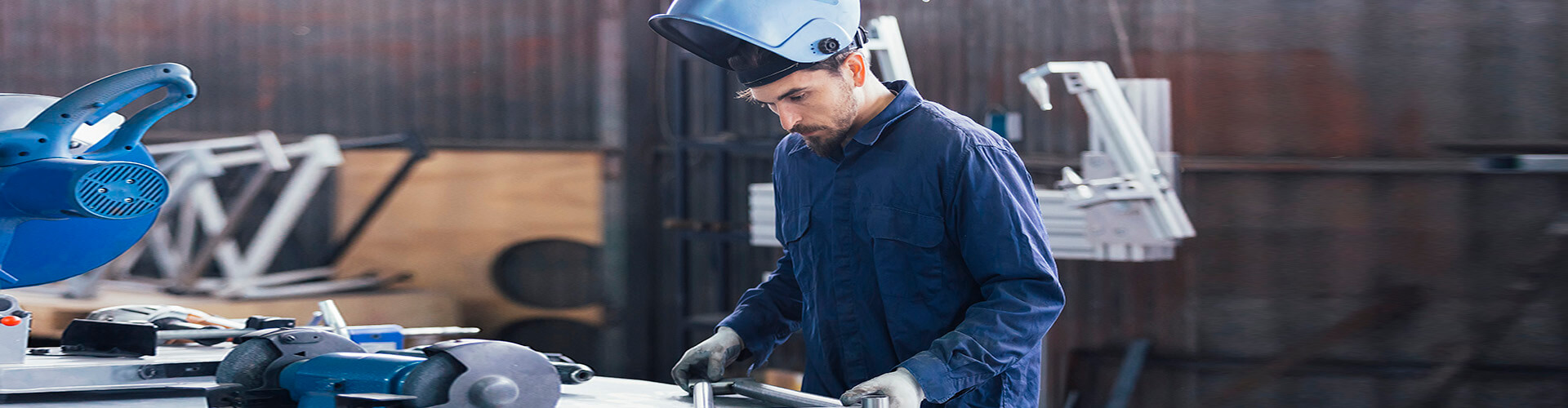  Seguro Multirriesgo Industrial - Hombre con casco y mono azul soldando metal en un taller