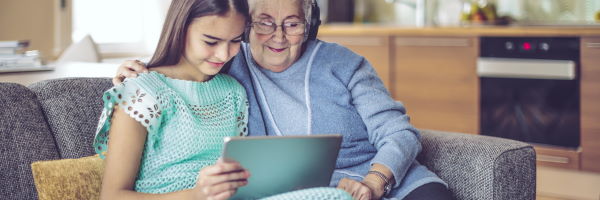 Qué tengo que hacer - Programa Pensión - Caja Rural de Navarra abuela-y-nieta-con-ropa-azul-sentadas-en-el-sofa-y-haciendo-una-videollamda-con-la-tablet.-auriculares
