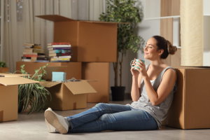 Chica tomando te en casa sentada en el suelo rodeada de cajas de mudanza