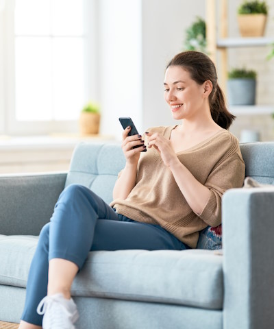 mujer-feliz-mirando-el-móvil-sentada-en-sofá-en-casa-Servicio Traslado de Cuenta de [dm:entidad]