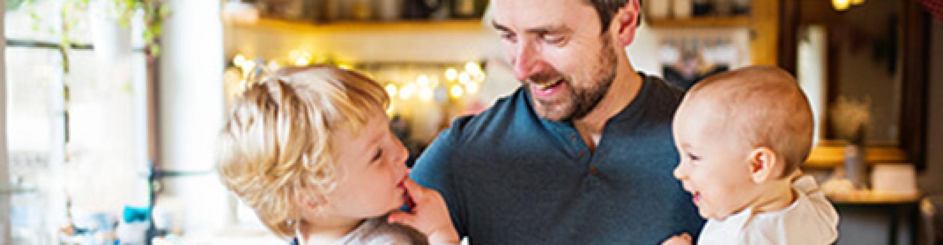 Padre con sus dos hijos en brazos en la cocina