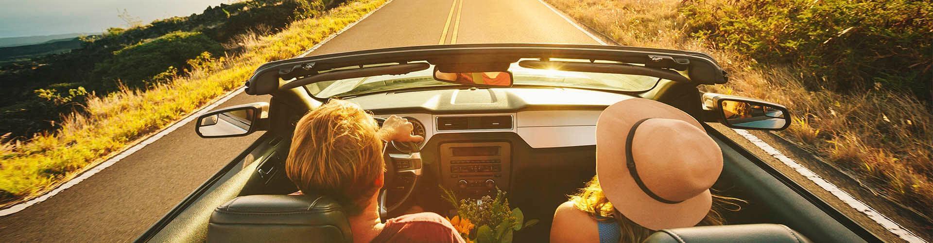 Seguro del Automóvil - Pareja feliz conduciendo por la carretera con su coche descapotable