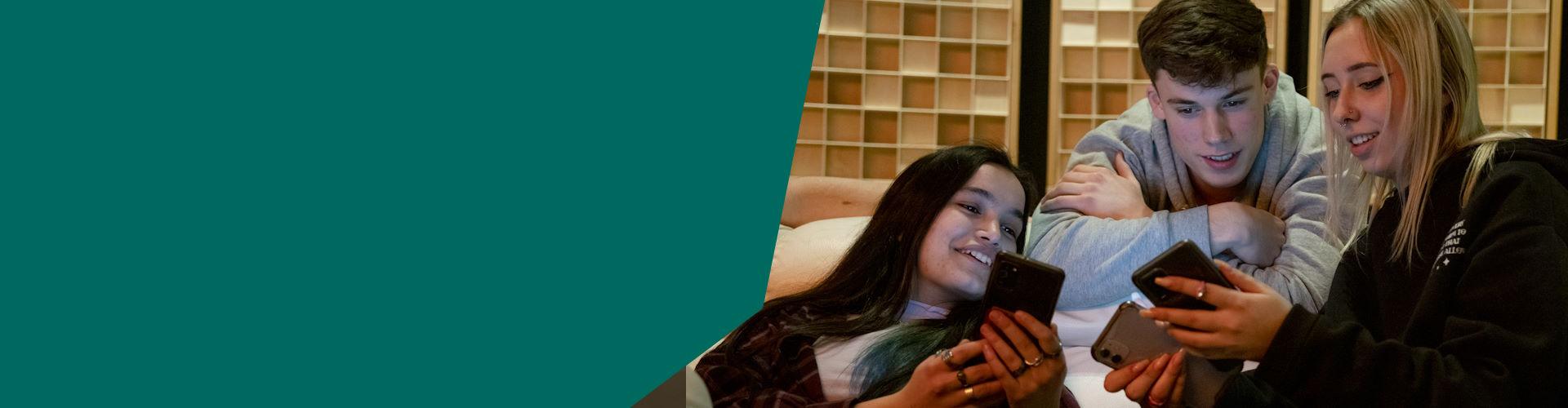 tres jóvenes en un sofá mirando sus móviles