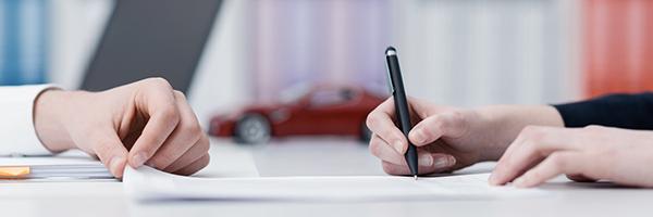 Renting de Automoción y Equipamientos - Manos firmando un contrato en una oficina con un coche de fondo Renting de Automoción y Equipamientos - Manos firmando un contrato en una oficina con un coche de fondo