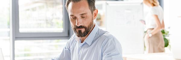 Programa Nómina - Manager de una empresa de mediana edad con barba y camisa azul trabajando en su portátil en la oficina Programa Nómina - Manager de una empresa de mediana edad con barba y camisa azul trabajando en su portátil en la oficina