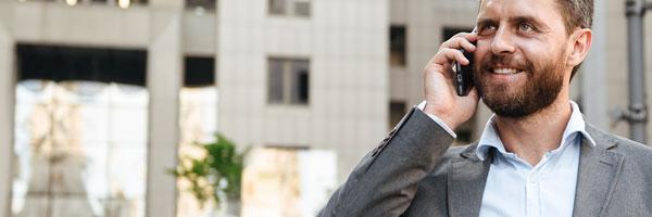 Seguros Banca Privada - Hombre de negocios con un traje gris y camisa blanca hablando por el móvil junto a un edificio en una ciudad