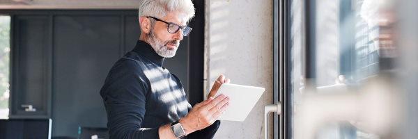 hombre-negocios-maduro-camiseta-negra-gafas-con-tablet-en-oficina-junto-ventana