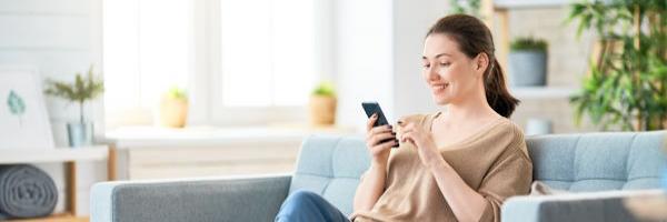 mujer-feliz-mirando-el-móvil-sentada-en-sofá-en-casa - 